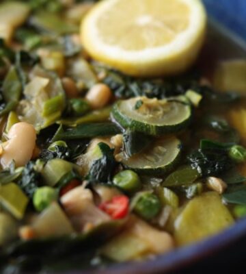 Vegan longevity stew with cannellini beans and leafy greens, served in a blue bowl and topped with a decorative lemon slice
