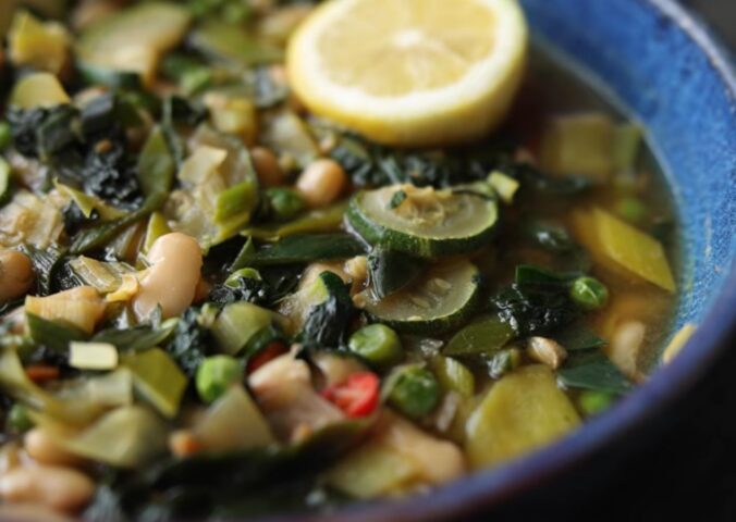 Vegan longevity stew with cannellini beans and leafy greens, served in a blue bowl and topped with a decorative lemon slice