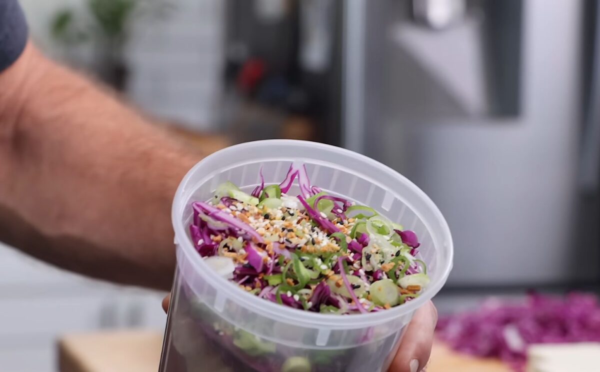Thompson holding a plastic container filled with his vegan cold noodle bowls for meal prep.