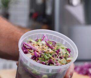 Thompson holding a plastic container filled with his vegan cold noodle bowls for meal prep.