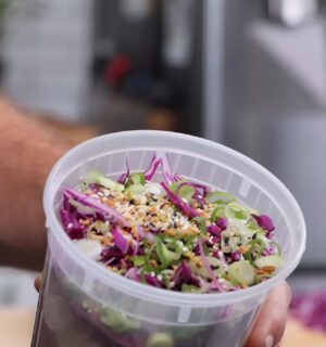 Thompson holding a plastic container filled with his vegan cold noodle bowls for meal prep.
