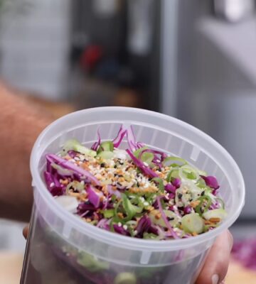 Thompson holding a plastic container filled with his vegan cold noodle bowls for meal prep.