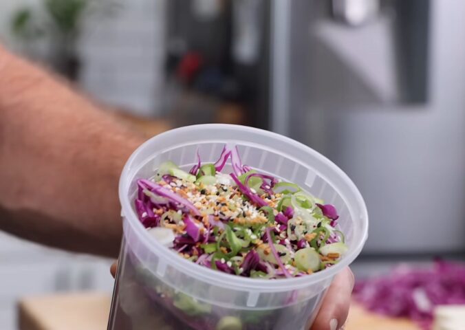 Thompson holding a plastic container filled with his vegan cold noodle bowls for meal prep.
