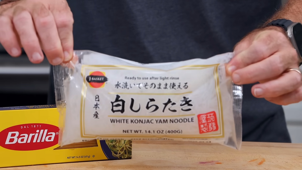 Thompson holding a bag of konjac noodles on his kitchen counter, where he also has a box of traditional pasta, as he explains how to prep his vegan cold noodle bowls