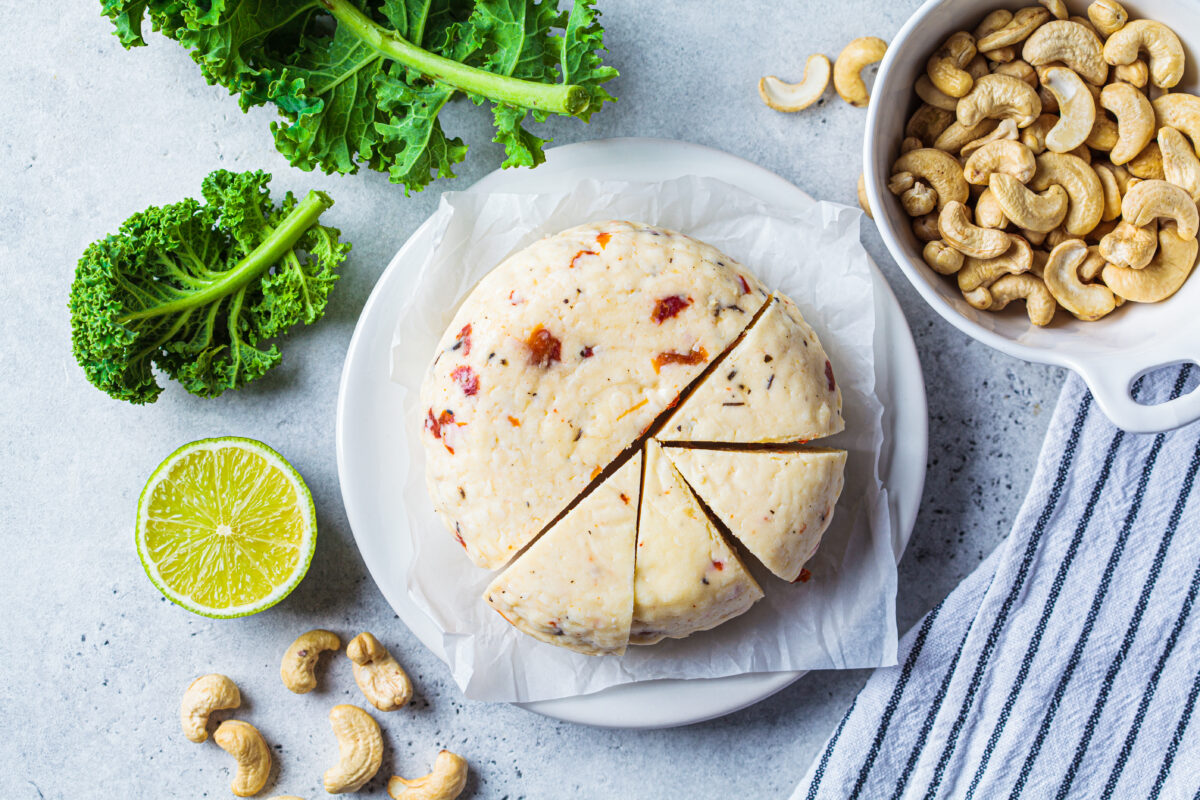Photo shows a large wheel of homemade vegan cheese next to a bowl of cashews. Scientists have managed to make a low-fat vegan cheese with ‘superior meltability.’
