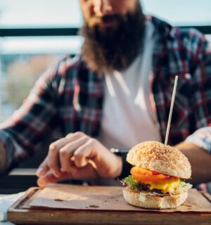 Photo shows a man with a beard about to eat a burger. Two new studies show that swapping processed meat for plant-based alternatives can significantly increase fiber intake and reduce salt and saturated fat consumption.