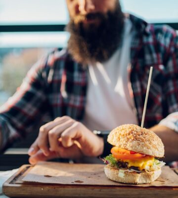 Photo shows a man with a beard about to eat a burger. Two new studies show that swapping processed meat for plant-based alternatives can significantly increase fiber intake and reduce salt and saturated fat consumption.