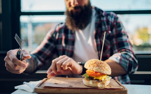 Photo shows a man with a beard about to eat a burger. Two new studies show that swapping processed meat for plant-based alternatives can significantly increase fiber intake and reduce salt and saturated fat consumption.
