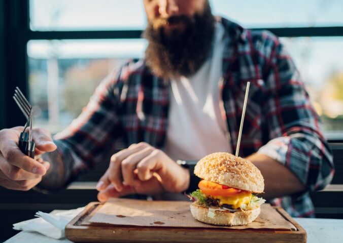 Photo shows a man with a beard about to eat a burger. Two new studies show that swapping processed meat for plant-based alternatives can significantly increase fiber intake and reduce salt and saturated fat consumption.