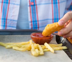 Photo shows a child dipping a chicken nugget into tomato ketchup on a tray with some french fries. The UK government is expected to announce a ban on fried foods such as chicken nuggets, battered fish and chips, and jam doughnuts in school dinners