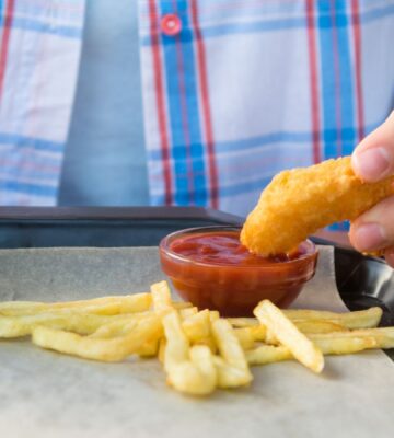 Photo shows a child dipping a chicken nugget into tomato ketchup on a tray with some french fries. The UK government is expected to announce a ban on fried foods such as chicken nuggets, battered fish and chips, and jam doughnuts in school dinners