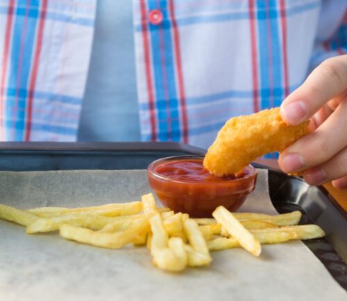 Photo shows a child dipping a chicken nugget into tomato ketchup on a tray with some french fries. The UK government is expected to announce a ban on fried foods such as chicken nuggets, battered fish and chips, and jam doughnuts in school dinners