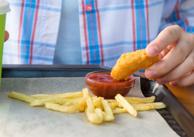 Photo shows a child dipping a chicken nugget into tomato ketchup on a tray with some french fries. The UK government is expected to announce a ban on fried foods such as chicken nuggets, battered fish and chips, and jam doughnuts in school dinners