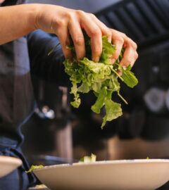 Photo shows someone in a dark uniform placing salad leaves into a bowl. UK prisons are now required to take imprisoned vegan people’s ethical beliefs into account while planning menus.