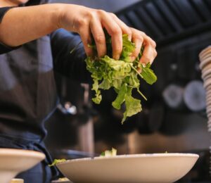 Photo shows someone in a dark uniform placing salad leaves into a bowl. UK prisons are now required to take imprisoned vegan people’s ethical beliefs into account while planning menus.