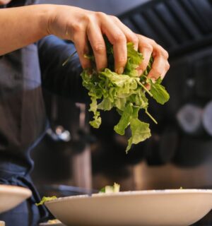 Photo shows someone in a dark uniform placing salad leaves into a bowl. UK prisons are now required to take imprisoned vegan people’s ethical beliefs into account while planning menus.