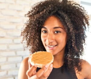 a picture of a woman in workout gear eating a peanut butter covered rice cake for a New Peanut Butter Study Finds Benefits For Muscle And Brain Health
