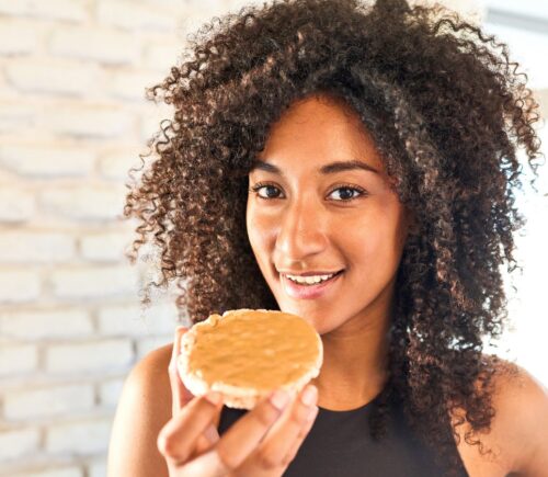 a picture of a woman in workout gear eating a peanut butter covered rice cake for a New Peanut Butter Study Finds Benefits For Muscle And Brain Health