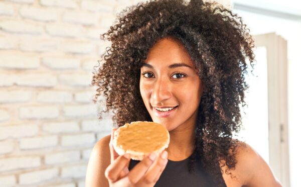 a picture of a woman in workout gear eating a peanut butter covered rice cake for a New Peanut Butter Study Finds Benefits For Muscle And Brain Health