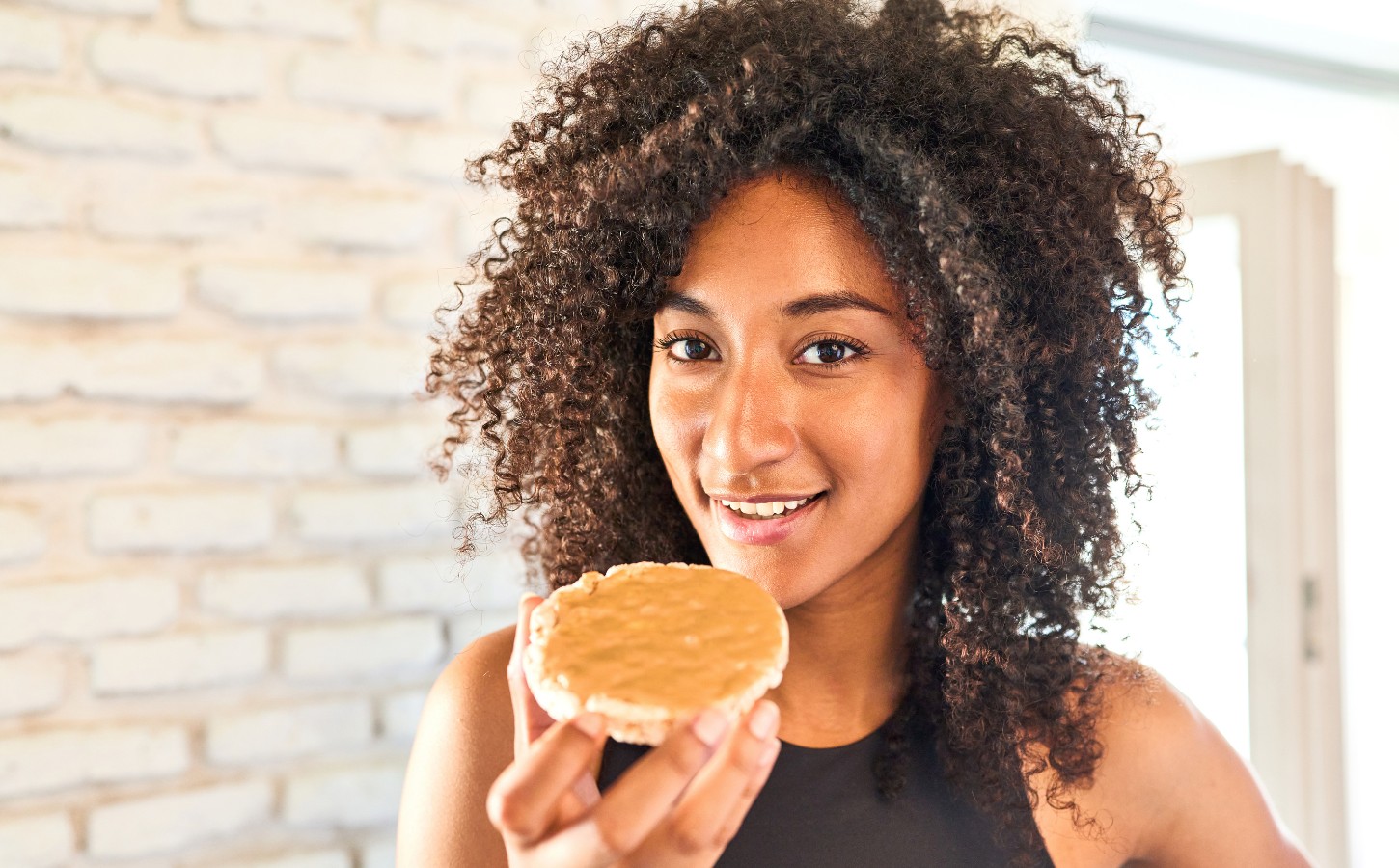 a picture of a woman in workout gear eating a peanut butter covered rice cake for a New Peanut Butter Study Finds Benefits For Muscle And Brain Health