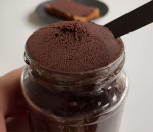 Glass jar of vegan chocolate chickpea spread with a slice of bread covered in the chocolate spread on a plate in the background