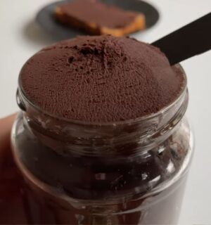 Glass jar of vegan chocolate chickpea spread with a slice of bread covered in the chocolate spread on a plate in the background