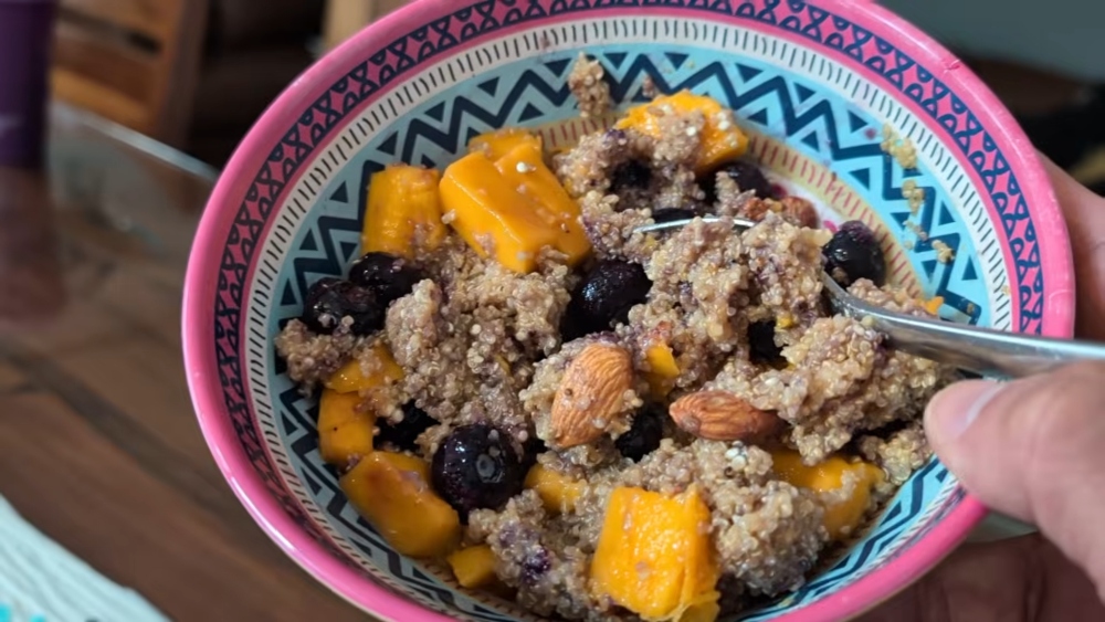 A colorful bowl of amaranth porridge topped with almonds, mango, and blueberries, showing how whole grains and healthy toppings can help build vegan protein