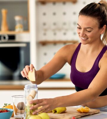 Sporty woman making a fruit smoothie on a kitchen island, to illustrate an article about meal timing health benefits.