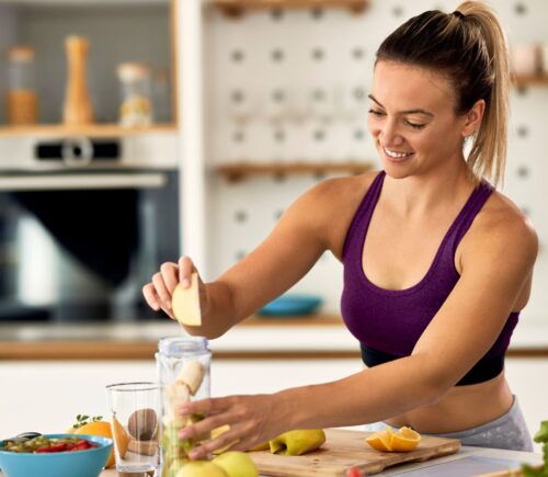 Sporty woman making a fruit smoothie on a kitchen island, to illustrate an article about meal timing health benefits.