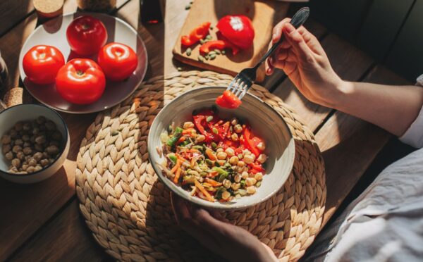 Photo shows someone eating a bowl of colorful plant-based foods at a sunny table. Adfree Cities says it is “proud” of backing the Ten Point Plan for Plant-Rich Diets.