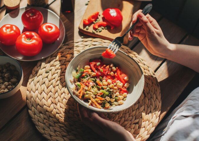 Photo shows someone eating a bowl of colorful plant-based foods at a sunny table. Adfree Cities says it is “proud” of backing the Ten Point Plan for Plant-Rich Diets.