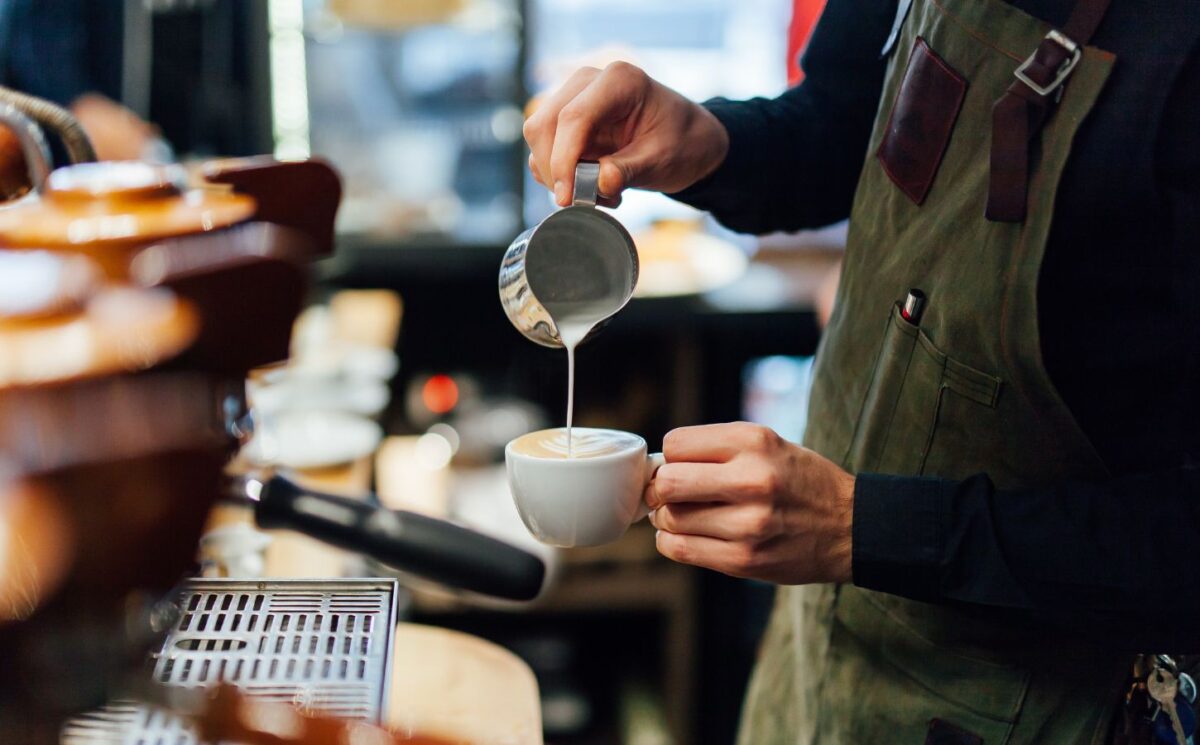 Photo shows a barista in a coffee shop or café pouring foamed milk into a cup of coffee. According to a new survey, the majority of UK coffee shops are open to making plant-based milk the default option