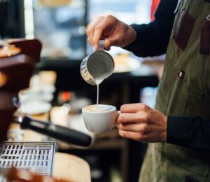 Photo shows a barista in a coffee shop or café pouring foamed milk into a cup of coffee. According to a new survey, the majority of UK coffee shops are open to making plant-based milk the default option
