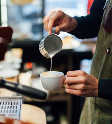 Photo shows a barista in a coffee shop or café pouring foamed milk into a cup of coffee. According to a new survey, the majority of UK coffee shops are open to making plant-based milk the default option