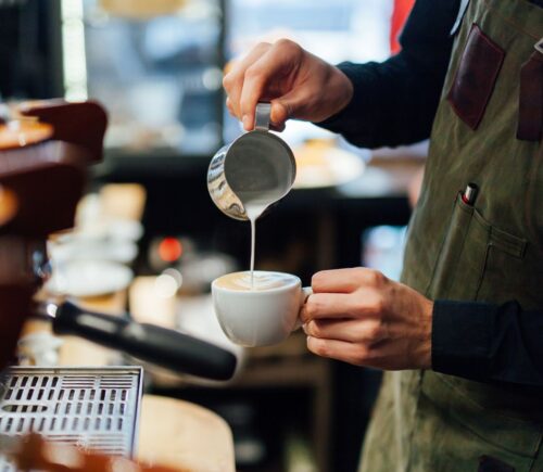 Photo shows a barista in a coffee shop or café pouring foamed milk into a cup of coffee. According to a new survey, the majority of UK coffee shops are open to making plant-based milk the default option