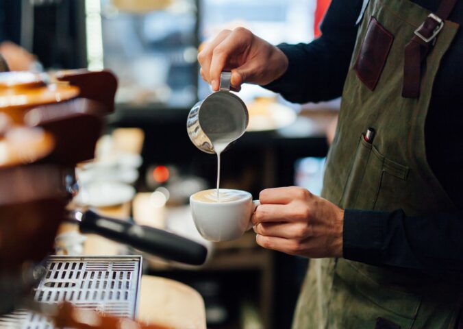 Photo shows a barista in a coffee shop or café pouring foamed milk into a cup of coffee. According to a new survey, the majority of UK coffee shops are open to making plant-based milk the default option