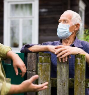 Photo shows two men in face masks talking over a wooden fence. Is factory farming already a public health crisis?