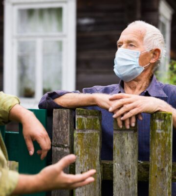 Photo shows two men in face masks talking over a wooden fence. Is factory farming already a public health crisis?