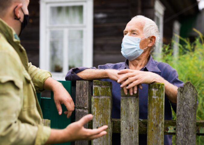 Photo shows two men in face masks talking over a wooden fence. Is factory farming already a public health crisis?