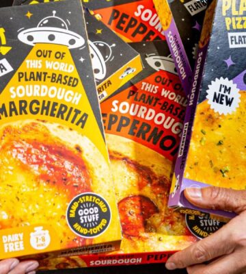 Photo shows Joe Hill, the co-founder of One Planet Pizza, holding a selection of the brand's frozen vegan pizzas and cheesy garlic bread. One Planet Pizza has passed £1 million in annualised retail sales for the first time ever