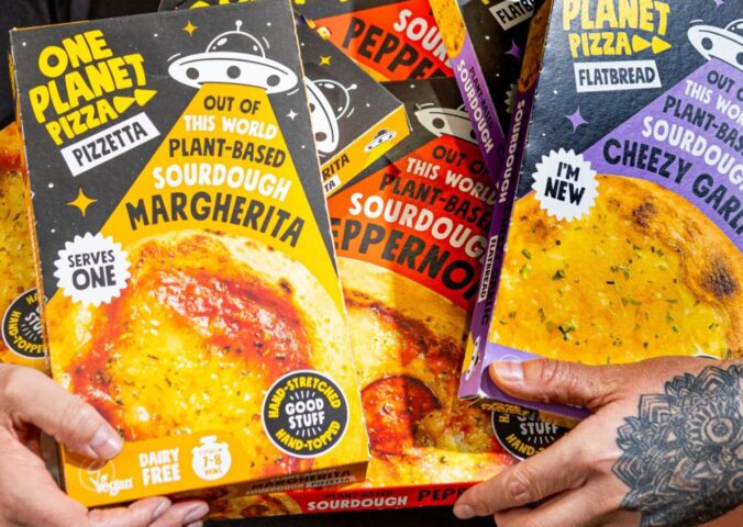 Photo shows Joe Hill, the co-founder of One Planet Pizza, holding a selection of the brand's frozen vegan pizzas and cheesy garlic bread. One Planet Pizza has passed £1 million in annualised retail sales for the first time ever