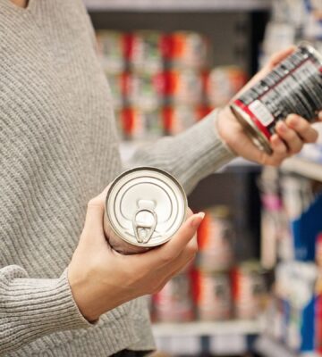 Photo shows a women holding up two cans of food in the supermarket and reading the packaging. A new study has found that people are more likely to say that they’re vegan than to actually follow a vegan diet
