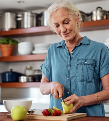 Photo shows an older woman cutting up an apple in her kitchen. A team of scientists has managed to reverse biological age in older adults using a four-week plant-forward diet