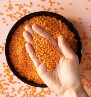 Photo shows someone taking a handful of dried red lentils from a bowl on a pink surface. Soy and legumes really can help to lower hypertension risk, according to a new study