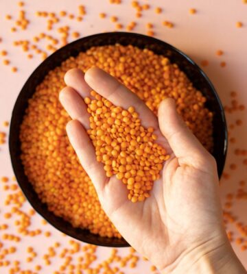 Photo shows someone taking a handful of dried red lentils from a bowl on a pink surface. Soy and legumes really can help to lower hypertension risk, according to a new study