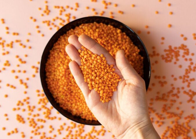 Photo shows someone taking a handful of dried red lentils from a bowl on a pink surface. Soy and legumes really can help to lower hypertension risk, according to a new study
