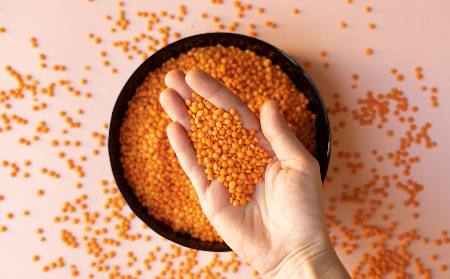 Photo shows someone taking a handful of dried red lentils from a bowl on a pink surface. Soy and legumes really can help to lower hypertension risk, according to a new study