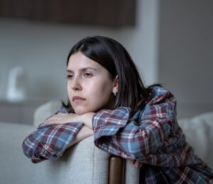 Pale woman sitting on a couch looking listlessly out the window, illustrating symptoms of low iron for article on how to fix low iron.
