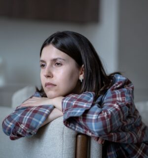 Pale woman sitting on a couch looking listlessly out the window, illustrating symptoms of low iron for article on how to fix low iron.