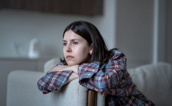 Pale woman sitting on a couch looking listlessly out the window, illustrating symptoms of low iron for article on how to fix low iron.